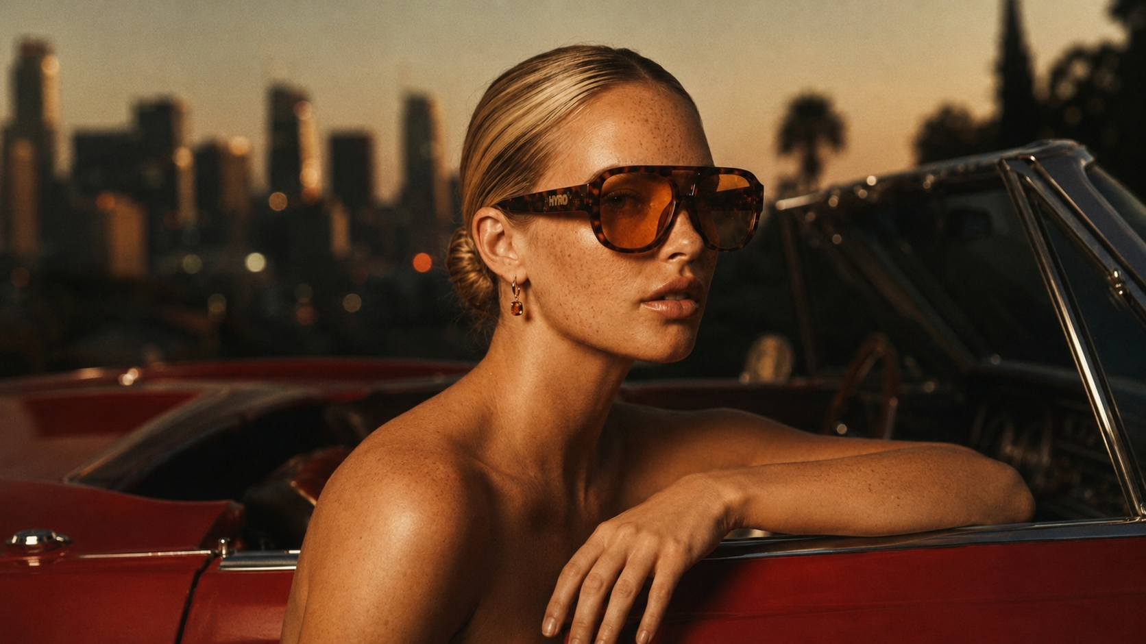 HYRO model wearing tortoise sunglasses in a convertible at sunset